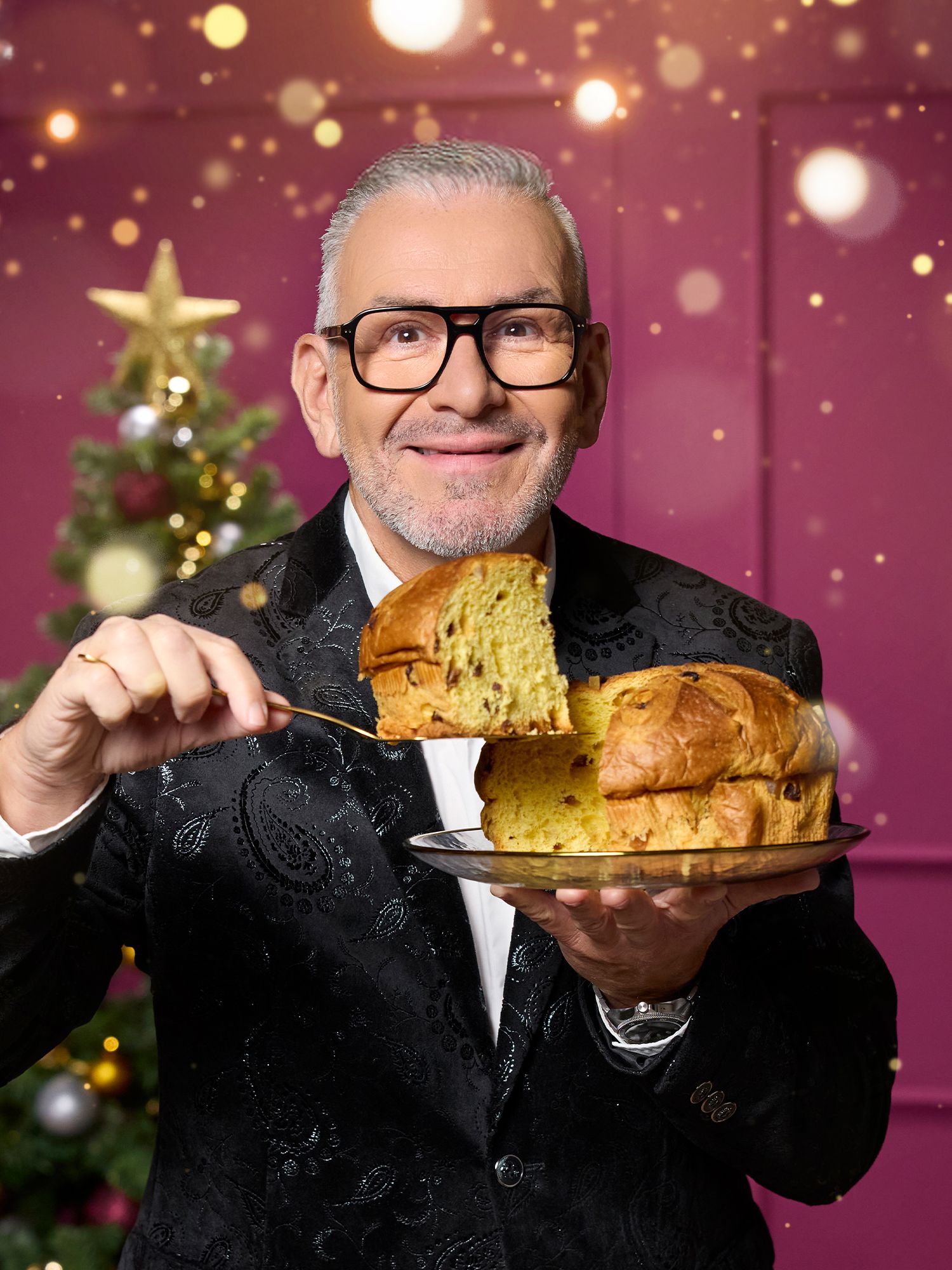 Festliche Köstlichkeiten Mann in schwarzem Sakko hält Teller mit aufgeschnittenem Panettone vor weihnachtlichem Hintergrund mit geschmücktem Baum.
