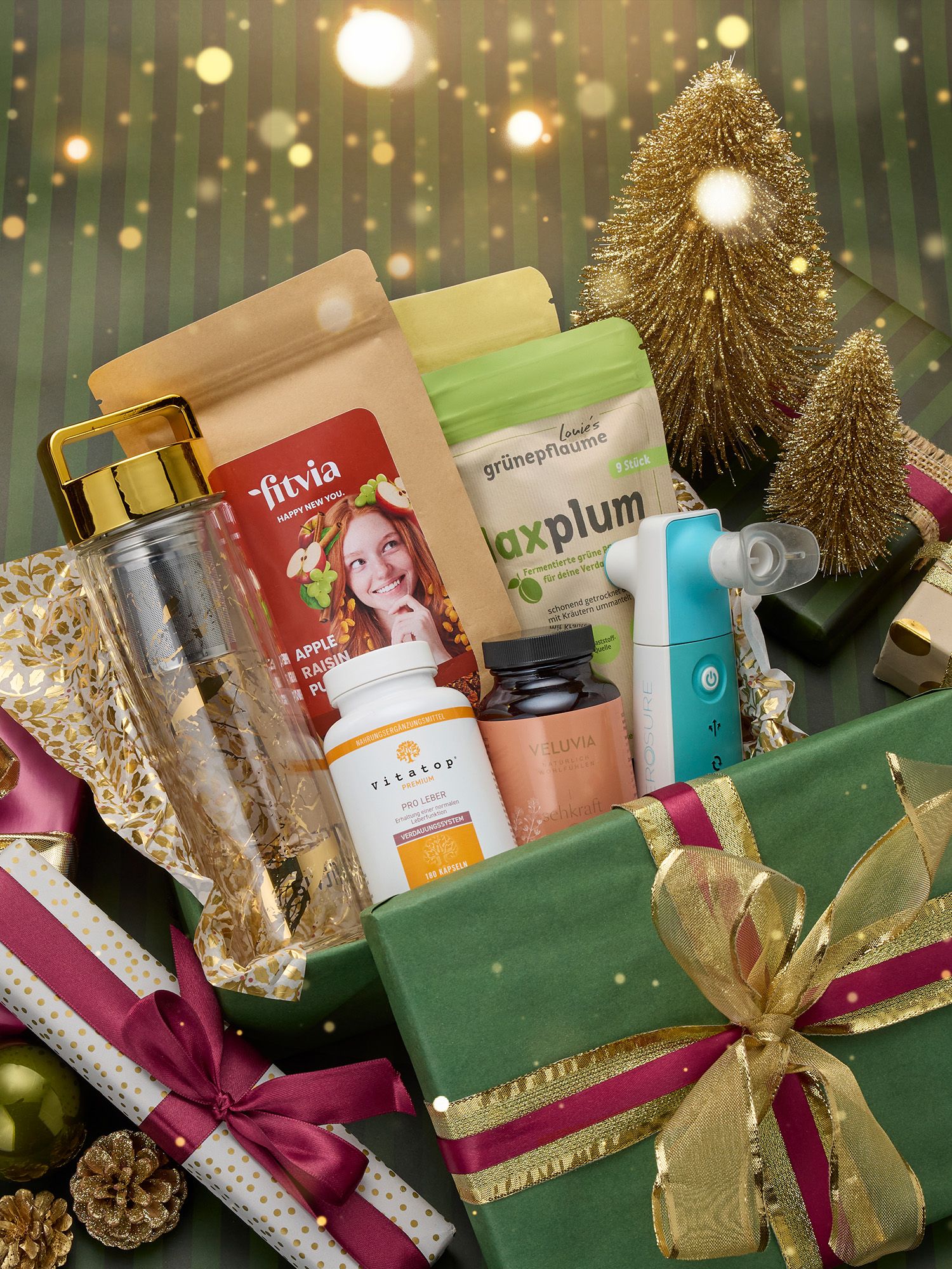 Gesundheit Geschenkbox mit grünem Papier und gold-rotem Band, gefüllt mit Trinkflasche, Nahrungsergänzungsmitteln, Inhalator und Snackverpackungen, umgeben von Weihnachtsdeko.