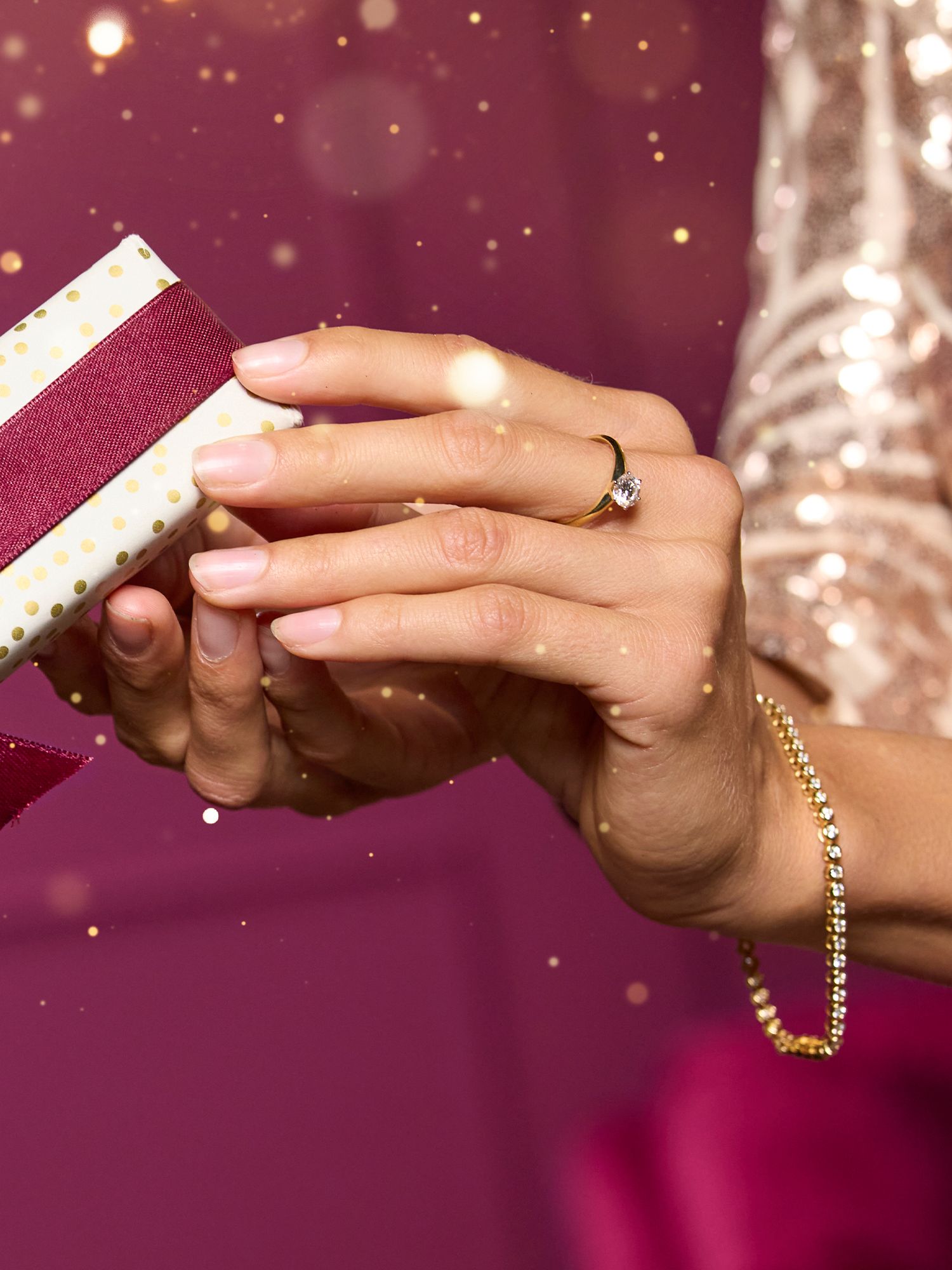 Festlicher Schmuck Hände mit goldfarbenem Ring und Armband halten Geschenk mit weißem Papier und dunkelrotem Band.