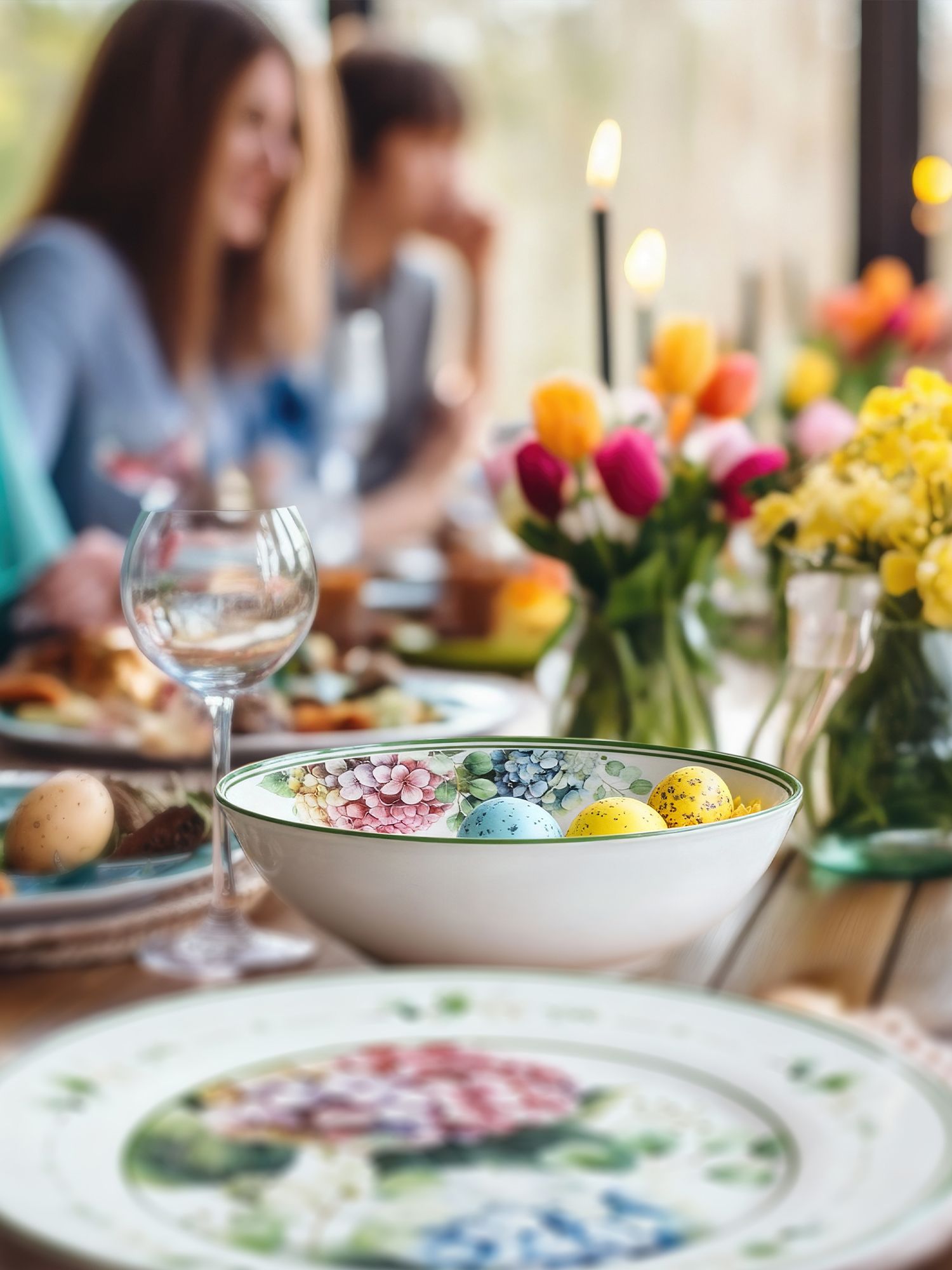 Ostertisch Ostertisch mit bunten Eiern in einer Schale, Blumenvasen und mehreren Personen im Hintergrund
