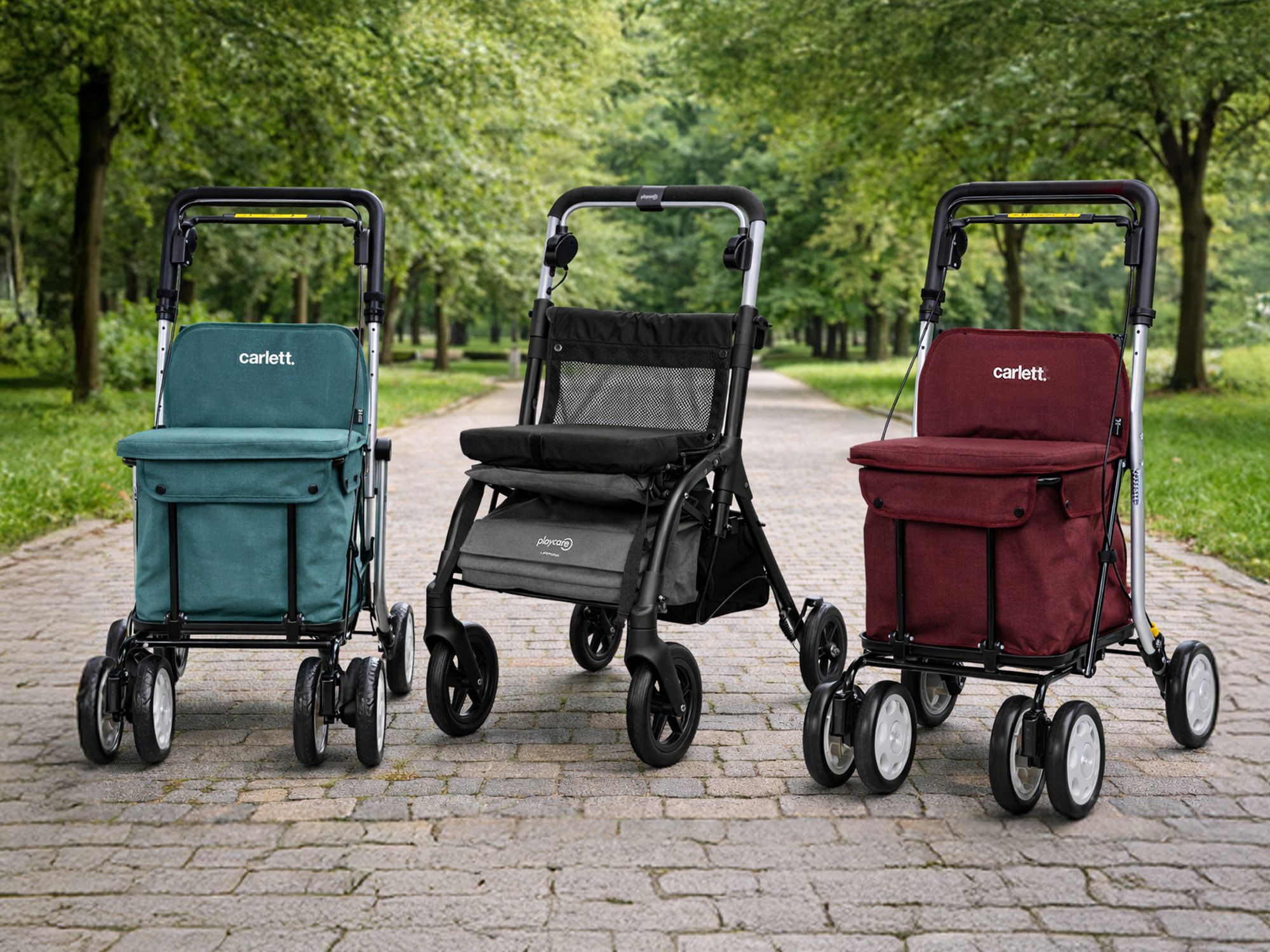 Drei Einkaufstrolley mit vier Rädern und Stofftaschen in Grün, Schwarz und Dunkelrot auf gepflastertem Weg im Park